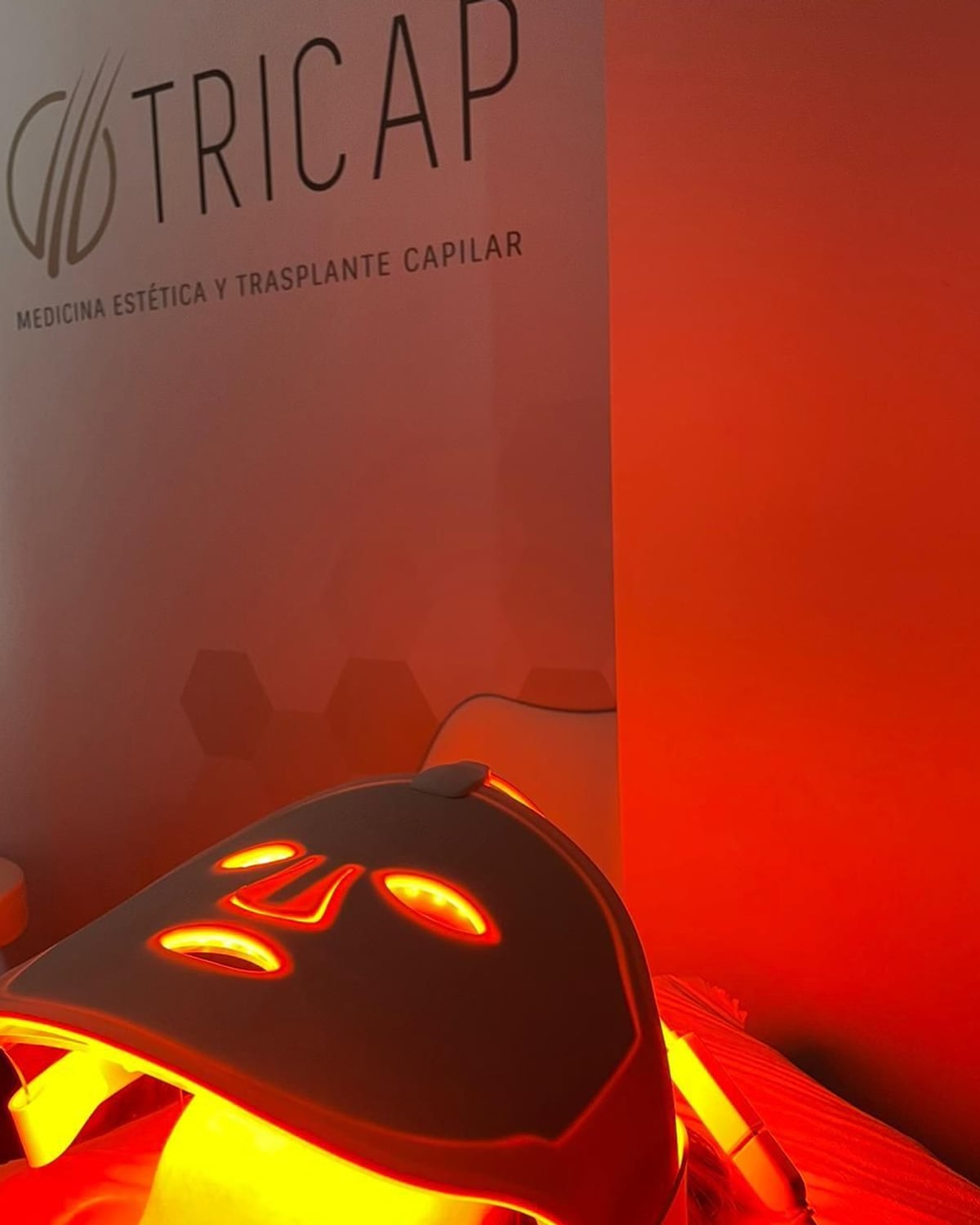 Cabina de medicina estética de Tricap: el rótulo de la clínica en la pared y una sesión con máscara LED
